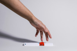 Hand reaching toward a finger-prick blood sample collection device, photograph.