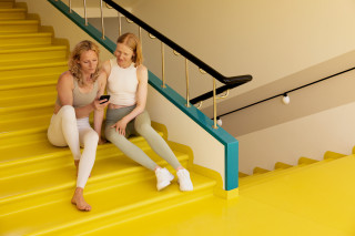 Two people seated on a staircase looking at a smartphone, photograph.