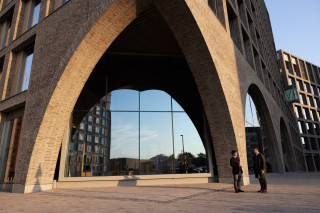 Modern office building with a large architectural archway and people walking outside, photograph.